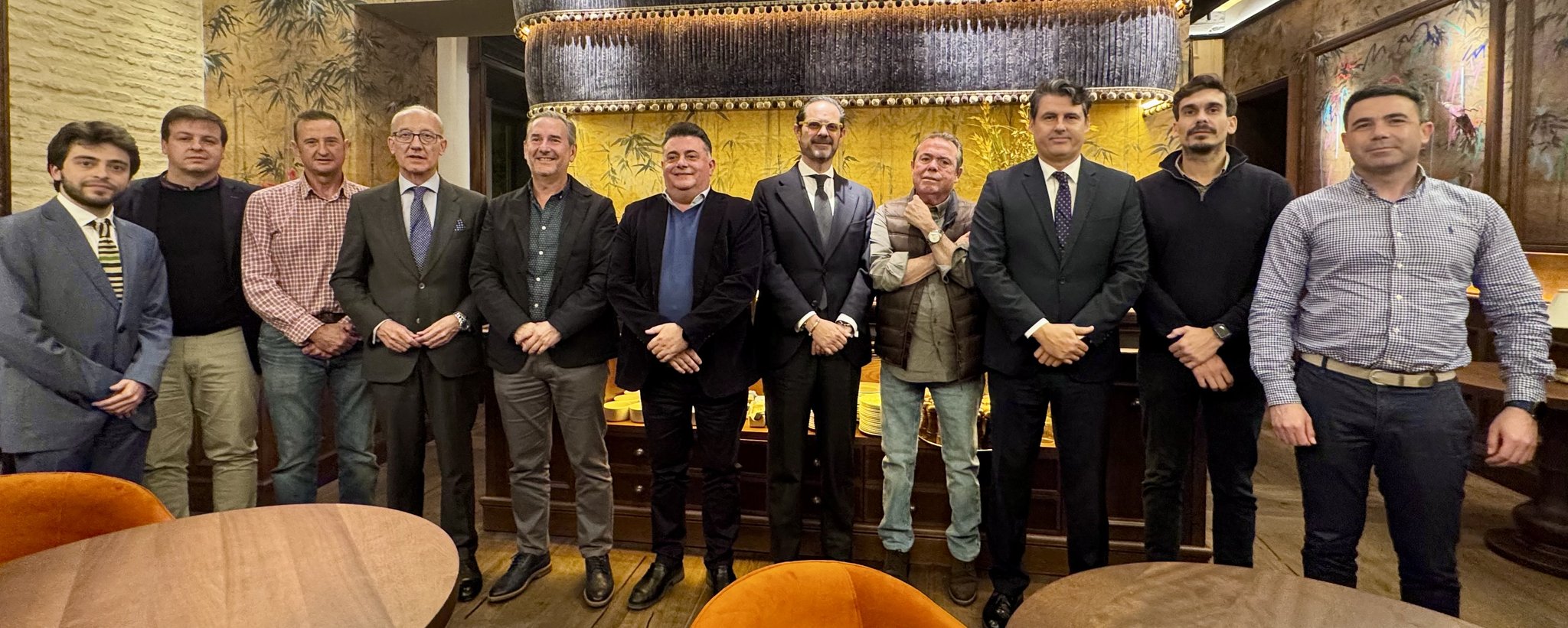 Grupo de once representantes de las organizaciones firmantes del I Convenio Colectivo del sector VTC de Andalucía posando de pie en un salón con mesas de madera y sillones naranjas